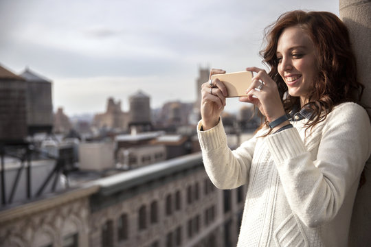 Smiling woman photographing with smart phone on balcony