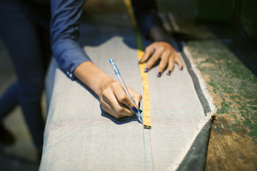 Female fashion designer marking on fabric with measuring tape