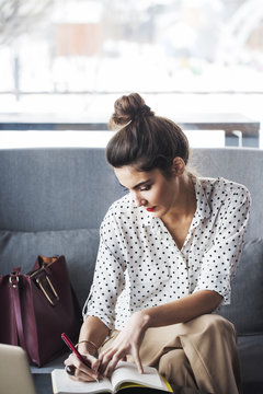A woman writing in a diary while sitting on sofa in the restaurant