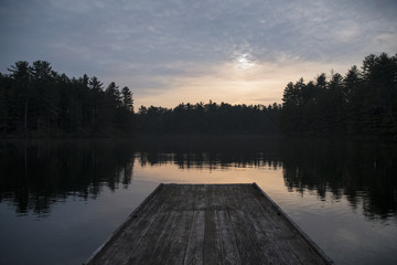 Pier on lake by silhouette trees against cloudy sky during sunset