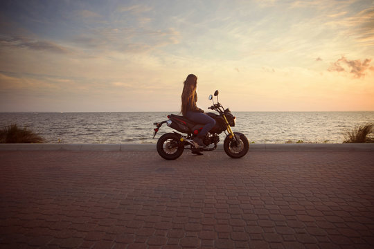 Side view of woman riding motorcycle on street against sea during sunset