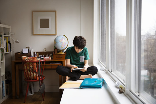 Boy using tablet while sitting by window at home