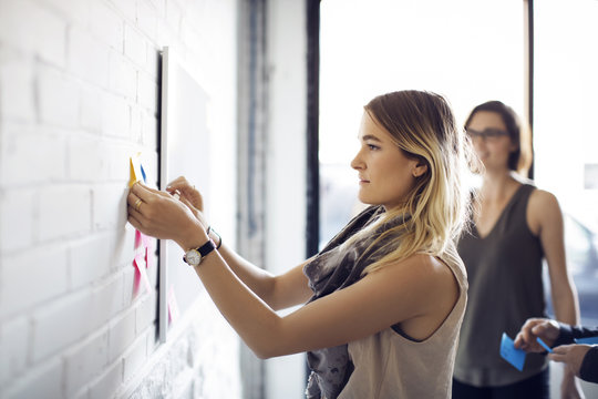 Businesswoman sticking notes on wall at creative office
