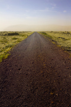 Dirt Road On Mossy Landscape Against Sky