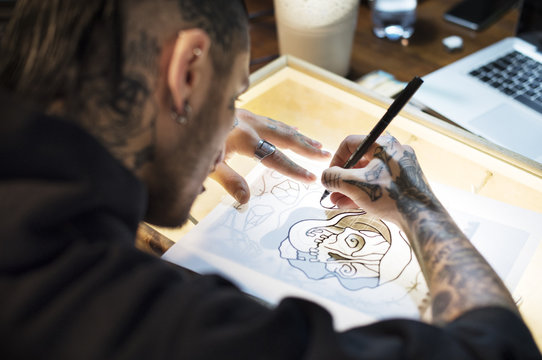 Young Tattoo Artist Drawing On Table In Studio