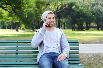 Young man talking on the phone  sitting on park bench.