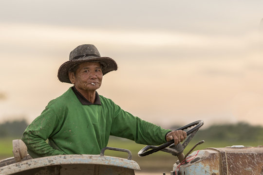 a senior male farmer smoking and sitting in a tractor during sun