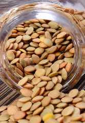 Lentil spilling out of glass jar. Wooden background