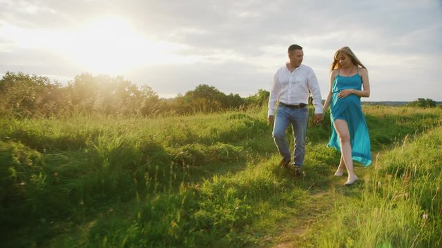 Steadicam shot: Young couple - husband and pregnant wife are going through the countryside at sunset