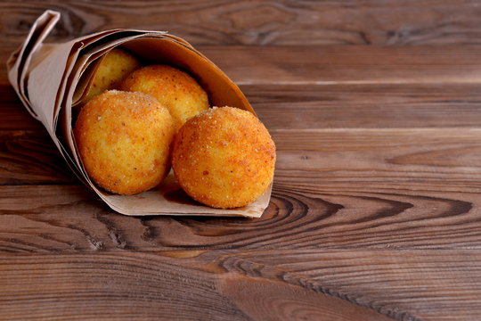 Arancini balls in paper on brown wooden background. Stuffed rice balls coated with bread crumbs and deep fried. Crispy and delicious snack, fast food