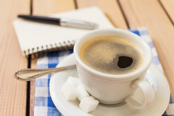 cup of coffee on a napkin and notepad with pen on wooden background
