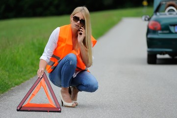 Junge blonde Frau hat eine Autopanne  und ruft mit dem Mobiltelefon Hilfe