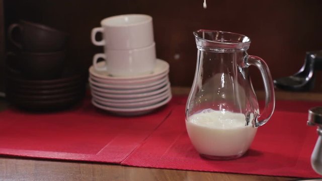 Barista pouring milk into a glass jug. Medium shot