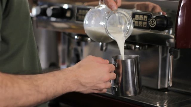 Barista pouring milk into a pitcher. Close up