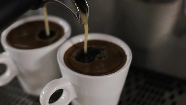 Two cups of espresso pour out. Close up