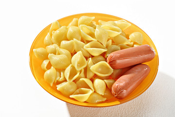 Cooked macaroni shells, served with sausage in orange plate on white background. Close up, high resolution product.