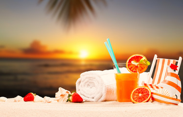 orange juice and summer accessories on sand with tropical beach background, summer concept, sun set