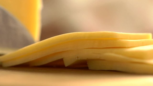 Slicing cheese into pieces closeup, super slow motion. Closeup shot of a piece of cheese. Somebody is cutting a serving of it with a knife