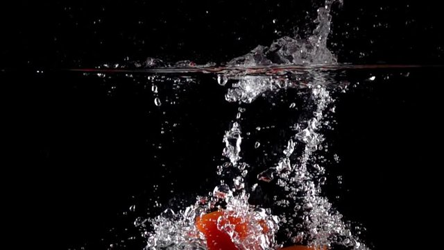 Super slow motion: four red tomatoes fall and float in water, black background