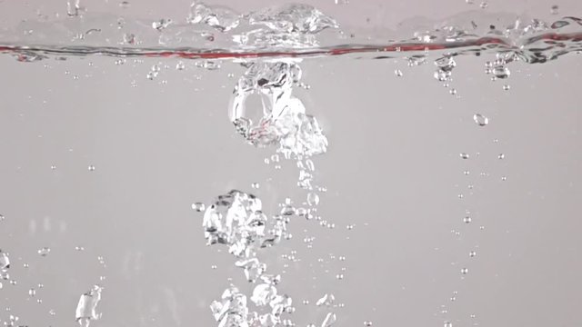 Red ripe tomatoes fall and float in water, grey background, high speed camera