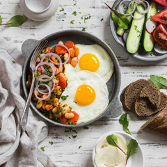 Delicious  breakfast or snack - a fried egg, beans in tomato sauce with onions and carrots, fresh cucumbers and tomatoes, homemade rye bread on light wooden background
