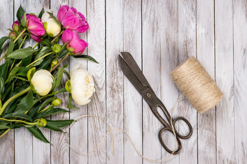 Bouquet of white and pink peonies flowers, twine and vintage scissors on white painted wooden planks.Top view.