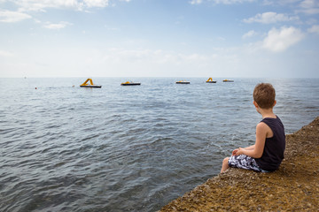 Child sitting on a pier and looking at the sea