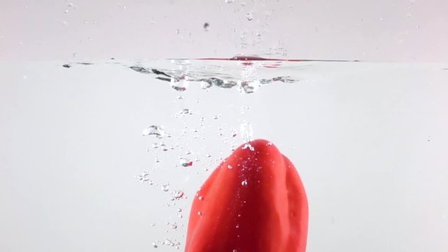 Red ripe bell pepper immersing in water, super slow motion, white background