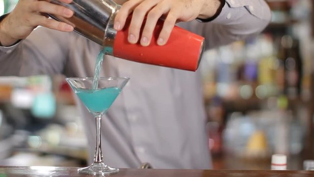 Bartender pours coctail from shaker into a glass. Medium shot
