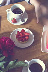 a cup of coffee in hand and cake with strawberry.cup of coffee and a dessert with strawberries, a female hand, in a cafe