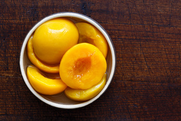 Canned peach halves in bowl isolated on dark background. From ab
