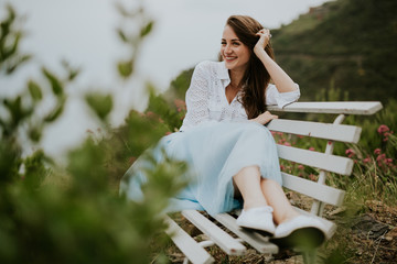 Naklejka premium Young cute smiling lady posing on a white chair in a beautiful place italy near ocean and mountains