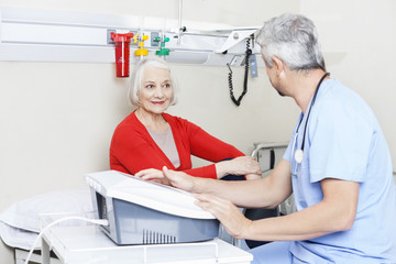 Obraz premium Senior Patient Looking At Male Physiotherapist Using Machine
