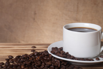 Coffee beans and coffee in white cup on wooden table opposite a