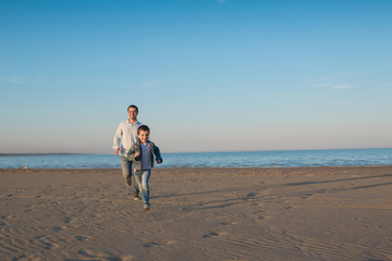 Father and his little son run on a beach in the evening
