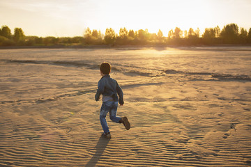 Little boy runs on a beach at the sunset