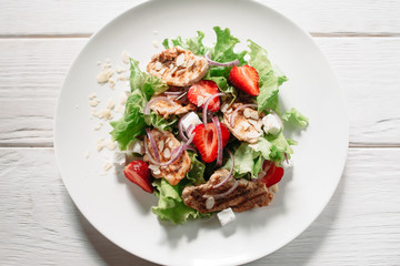 Tasty meat salad with mozzarella, strawberry and onion flat lay on white wooden background. Top view on meal of meat steaks, lettuce, strawberry, onion and mozzarella on white plate.