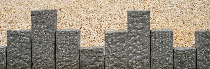 Dunkelgraue Stelen aus Granit vor beigefarbenem Steingranulat im Panoramaformat

- - - Dark gray steles made of granite before beige stone granules in panoramic format
