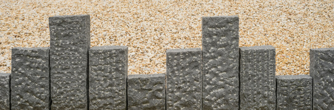 Dunkelgraue Stelen aus Granit vor beigefarbenem Steingranulat im Panoramaformat

- - - Dark gray steles made of granite before beige stone granules in panoramic format

