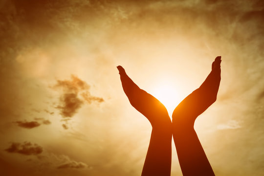 Raised hands catching sun on sunset sky. Concept of spirituality, wellbeing, positive energy