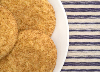 Fresh baked snickerdoodle cookies on a plate atop a blue striped tablecloth.