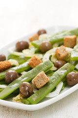 salad green beans with olives and croutins on white dish on white background