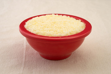 Small bowl of grated Pecorino Romano cheese on a beige tablecloth.