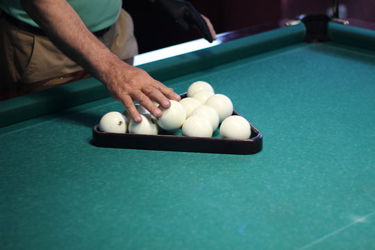 Hands of man folding white billiard balls in triangle on green billiard table