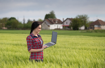 Naklejka na ściany i meble Farmer girl with laptop in field