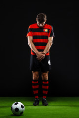 Soccer player with ball standing over black background