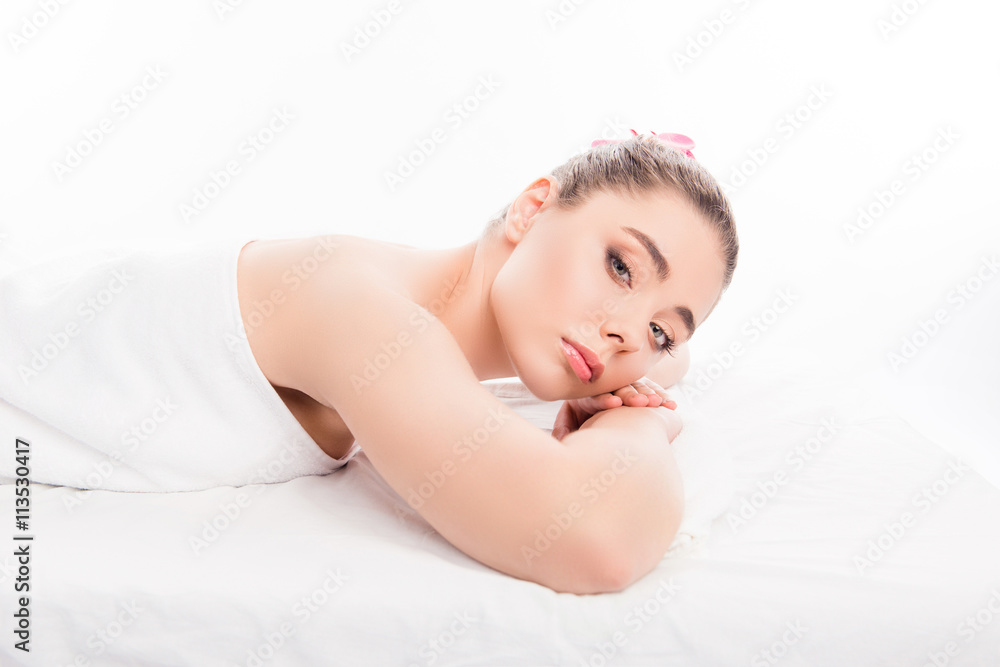 Wall mural Portrait of young woman lying in spa salon with orchid in her ha