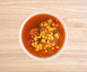 Corn okra and tomatoes soup in a white bowl on a wood table top view.