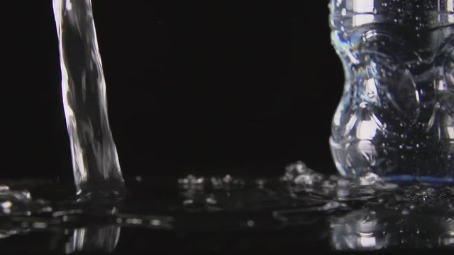 SLOW MOTION: A water flow falls on a black table near a plastic bottle