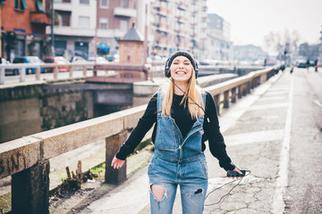 Knee figure of young beautiful blonde straight hair woman in the city listening music with headphones, laughing - music, having fun, happiness concept